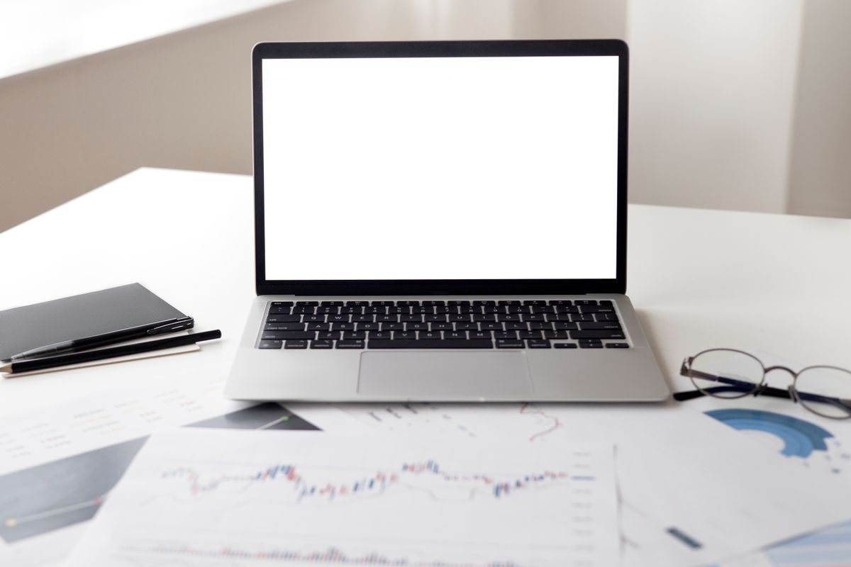 Open laptop with financial documents and charts spread across a desk