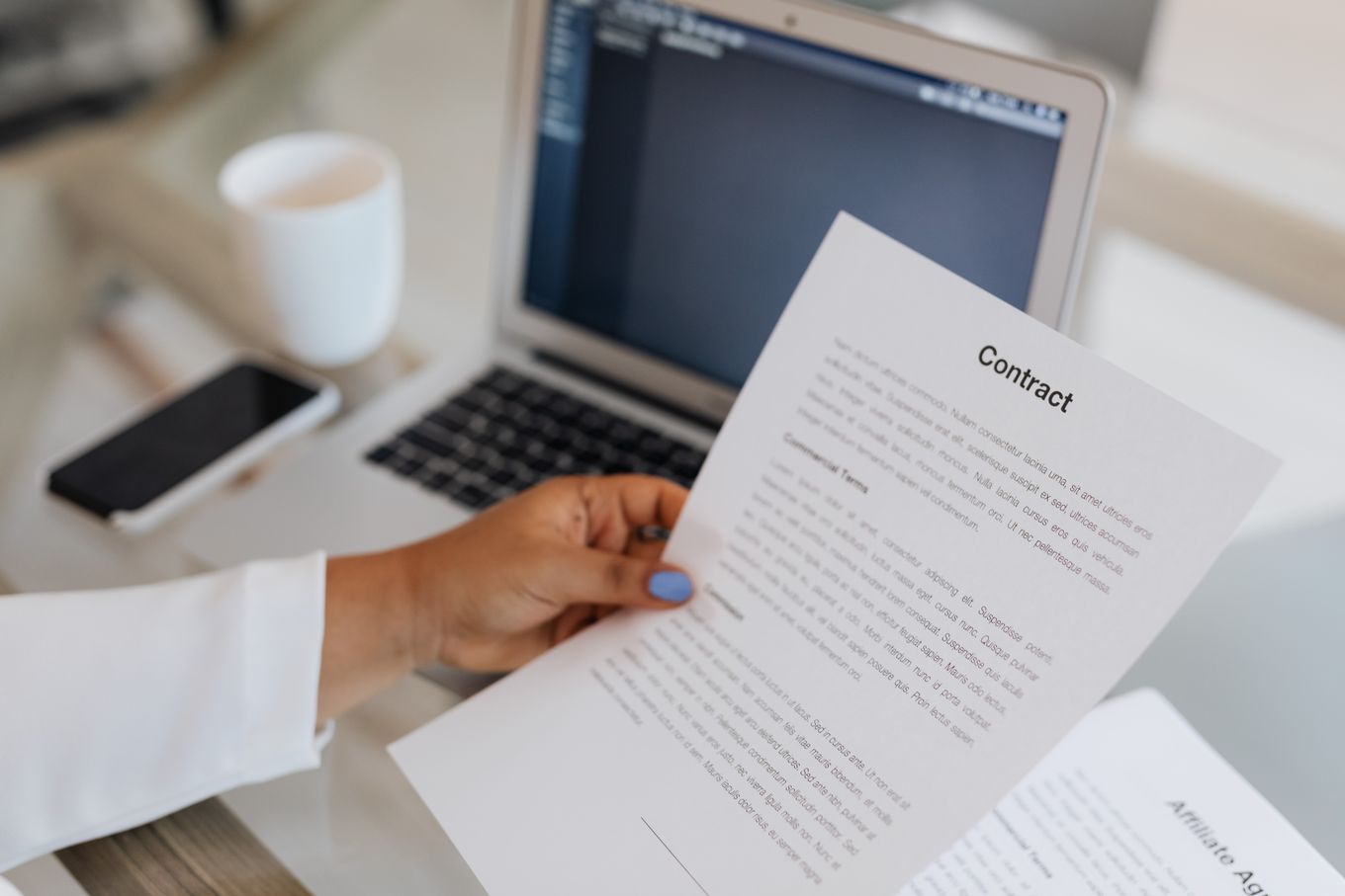 Hand holding a printed contract next to an open laptop