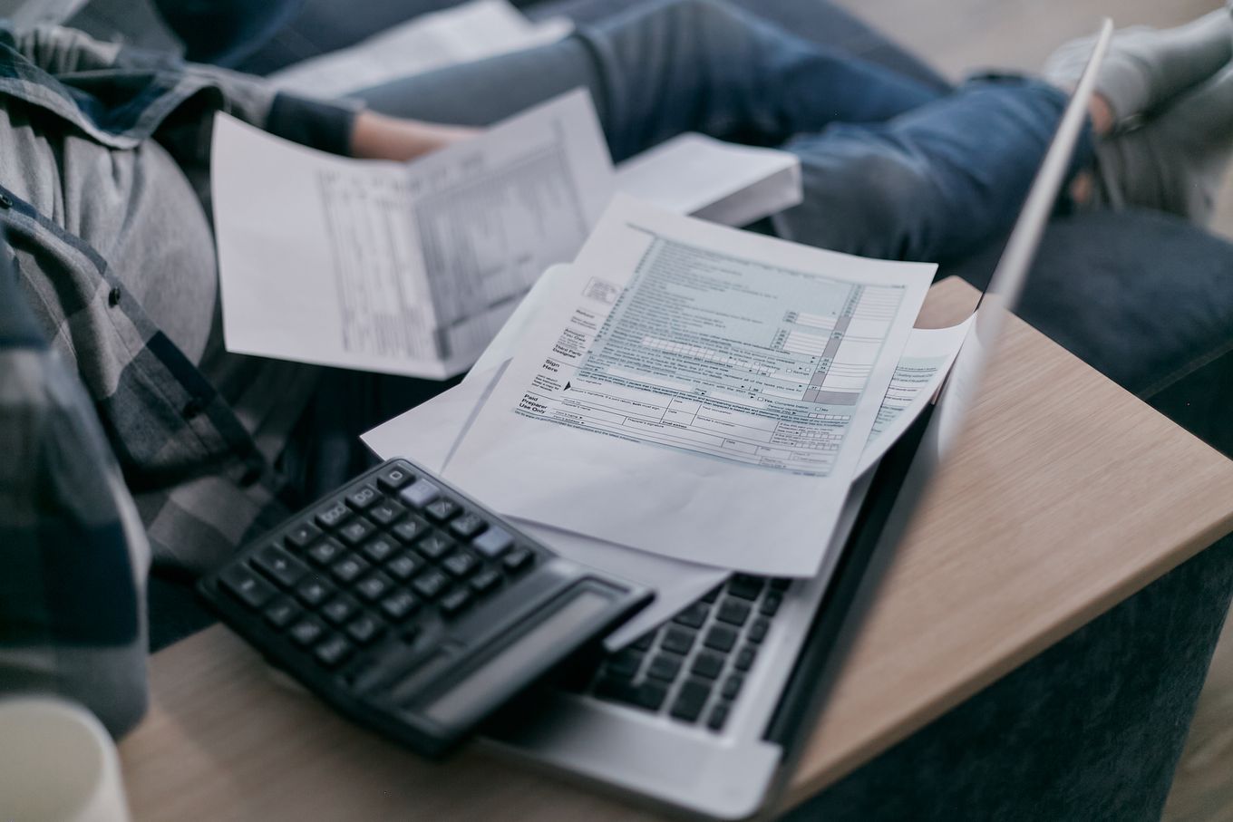 Tax forms, a calculator and a laptop spread across a lap at home