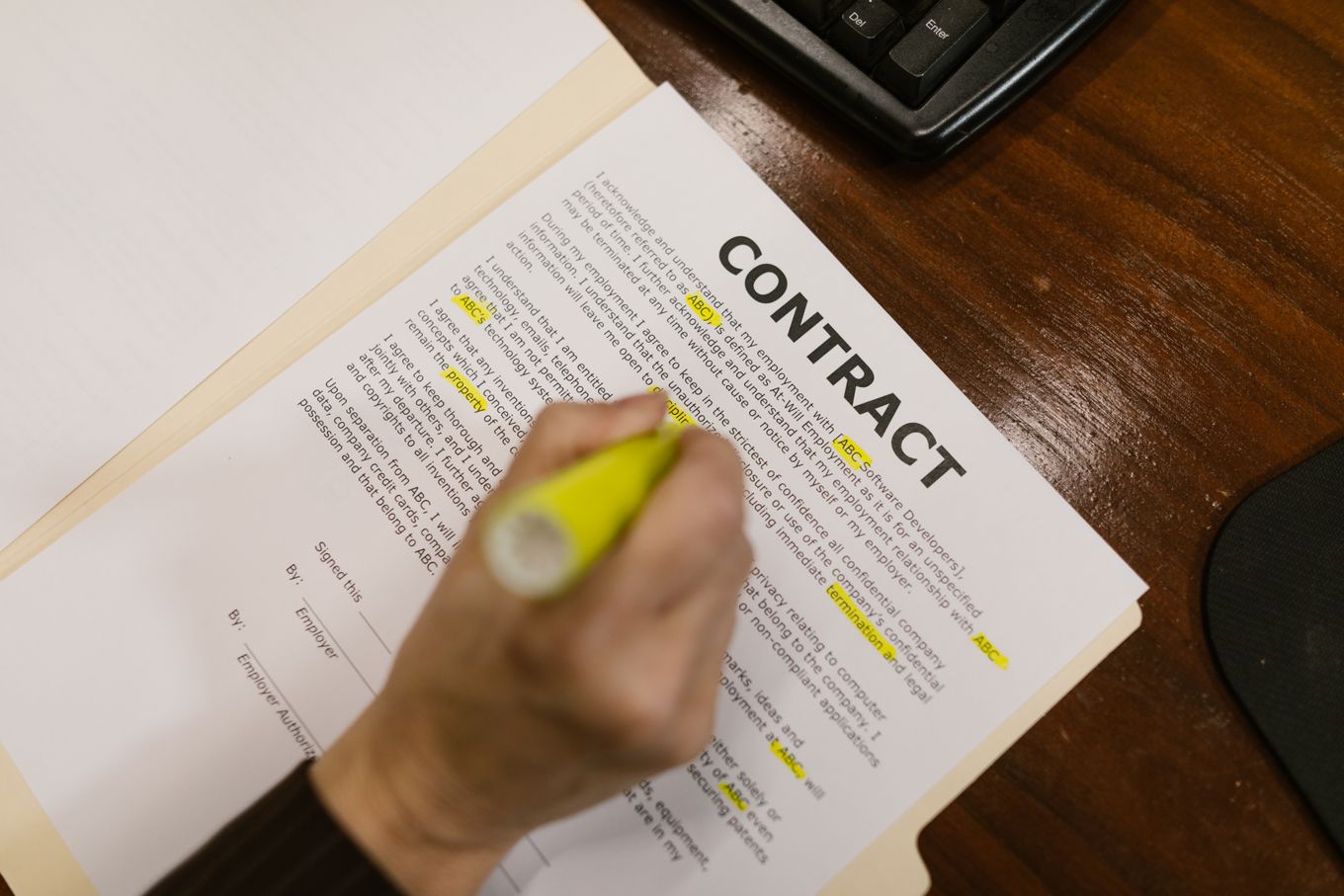 Hand highlighting clauses in a printed contract on a wooden desk