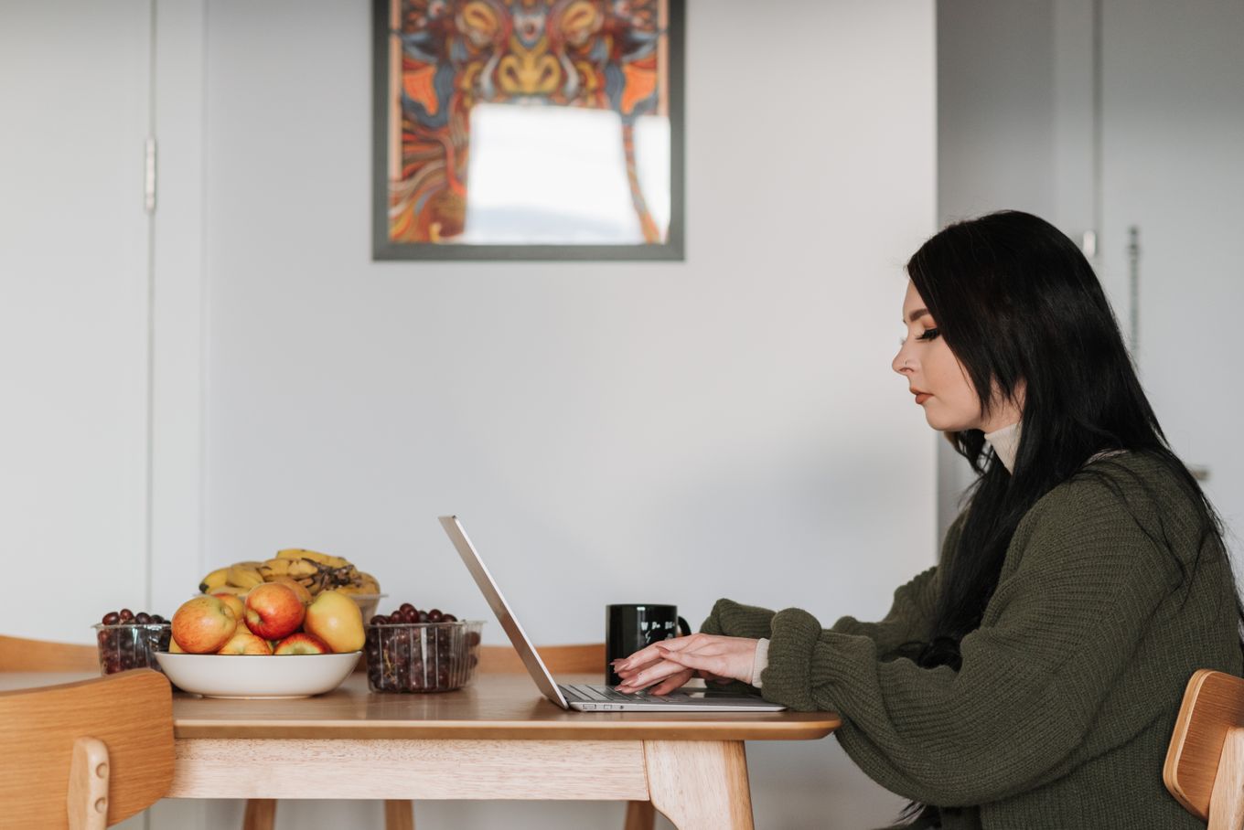 Freelancer typing on a laptop at a kitchen table with a bowl of fruit