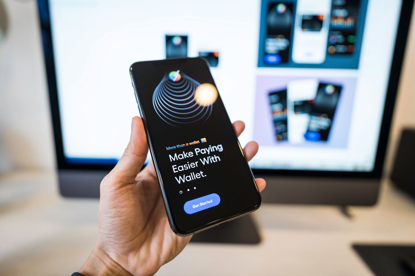 Hand holding a smartphone showing a digital wallet app in front of a computer screen