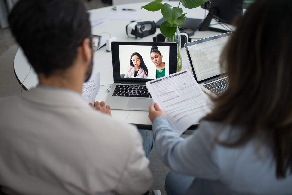 Two colleagues interviewing a remote candidate over a video call on a laptop