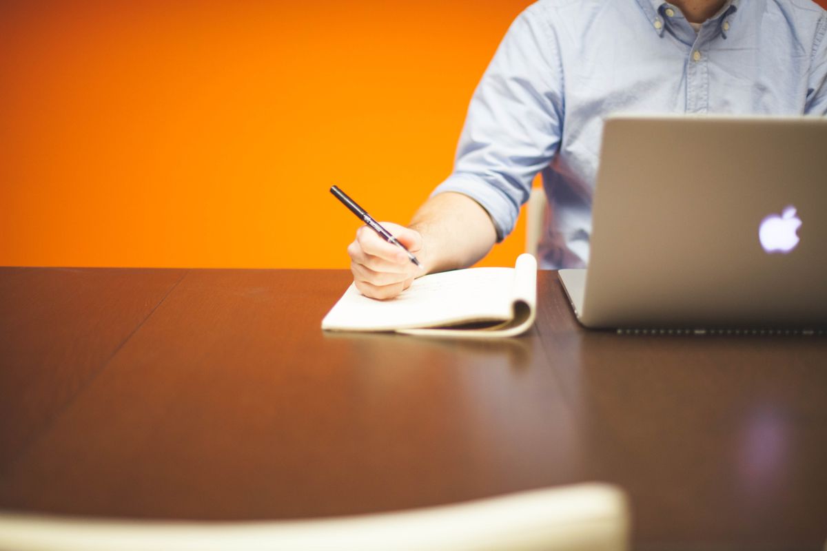 Freelancer writing notes beside a laptop while calculating rates