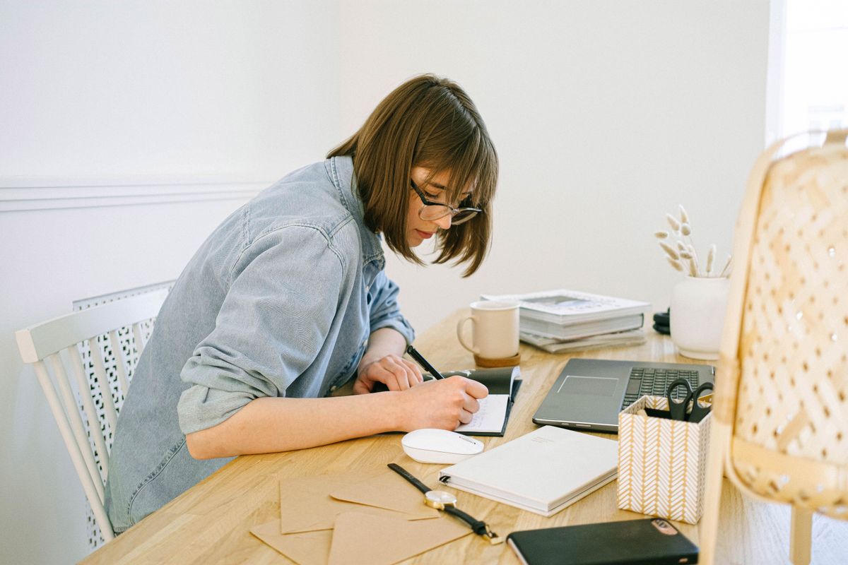 Freelancer writing a note at a home desk with a laptop