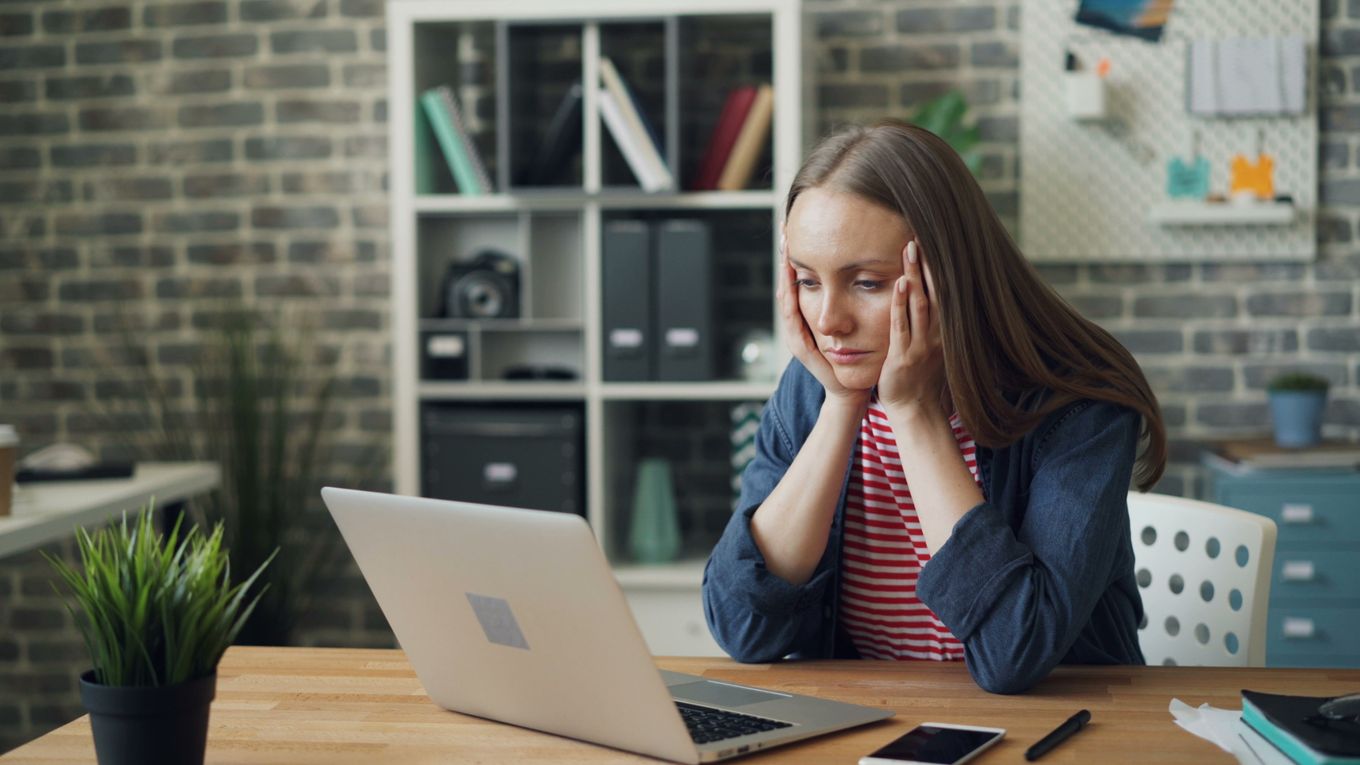 Freelancer at a laptop reading a message with a worried expression