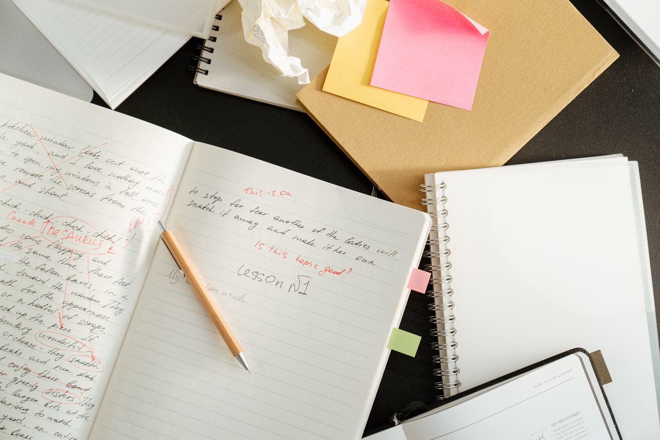Handwritten drafts with red-pen edits and sticky notes on a desk