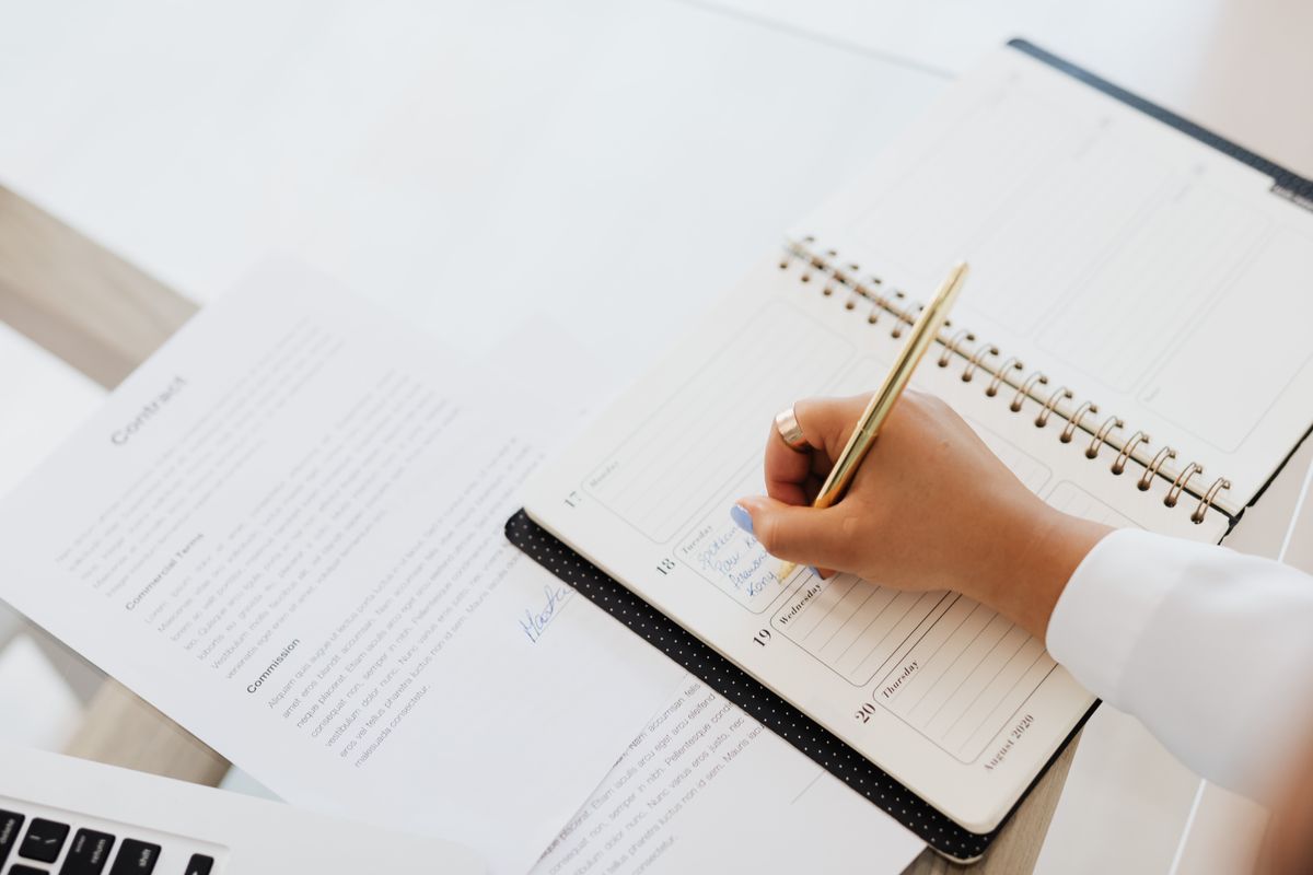 Close-up of a person writing in a planner next to a contract document on a desk