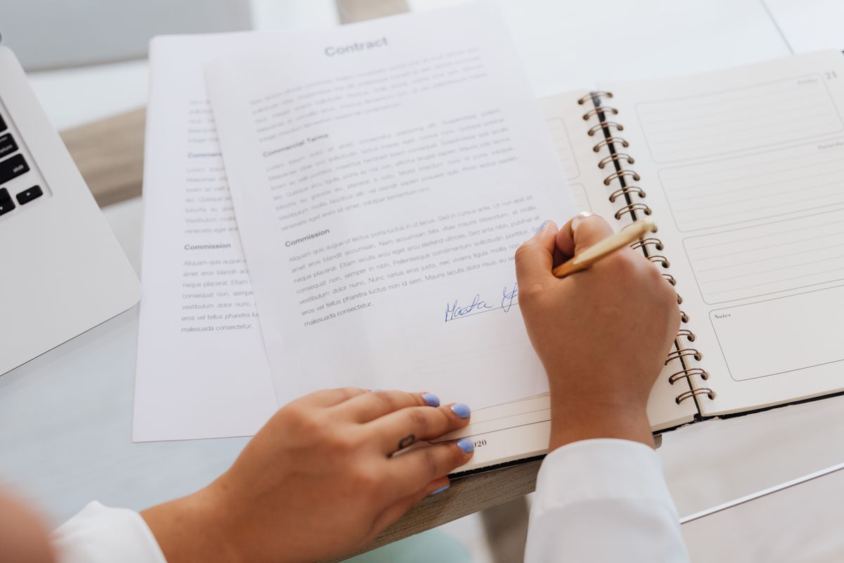 Close-up of hands signing a contract on a desk with office supplies