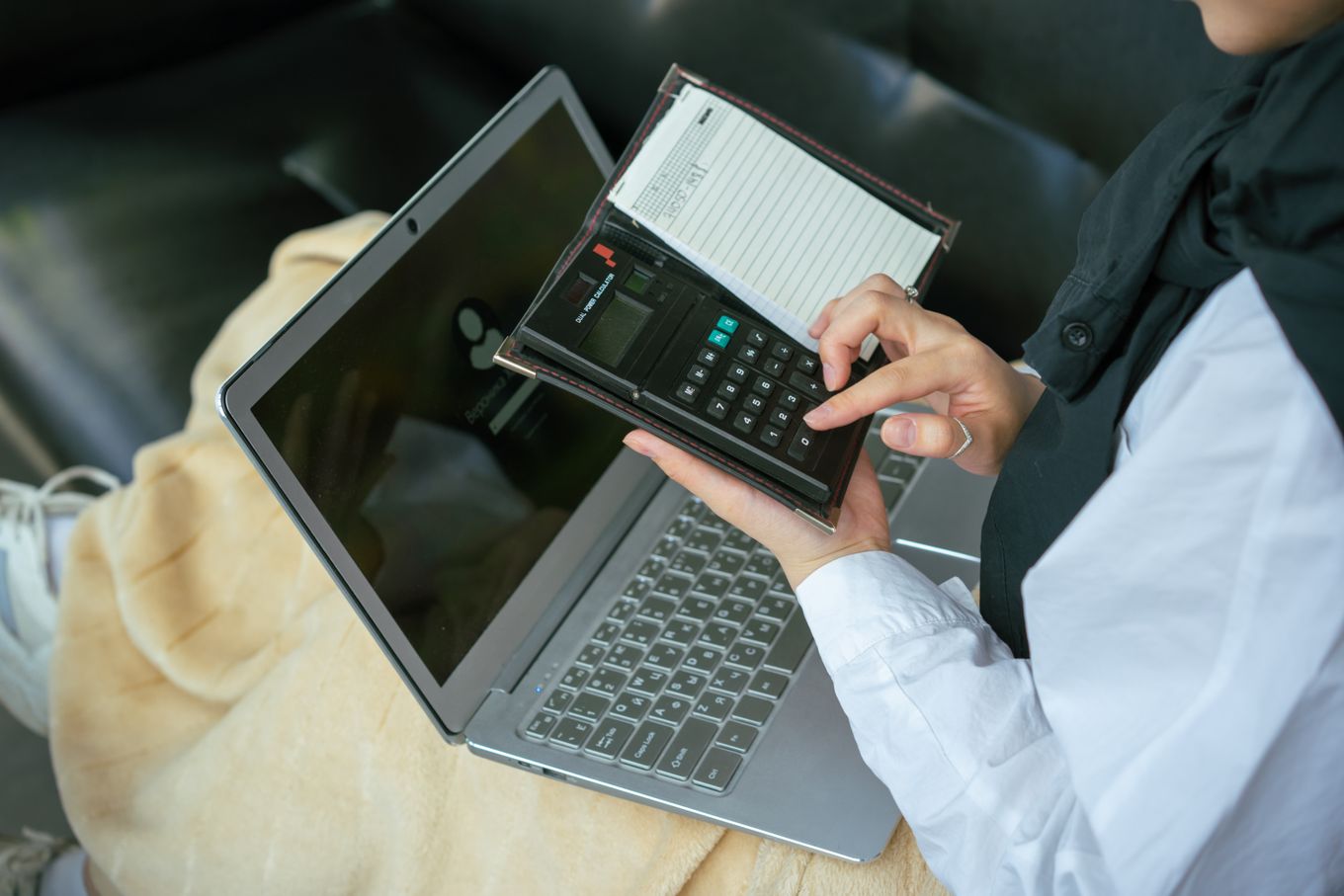 Person working out figures on a calculator held over an open laptop