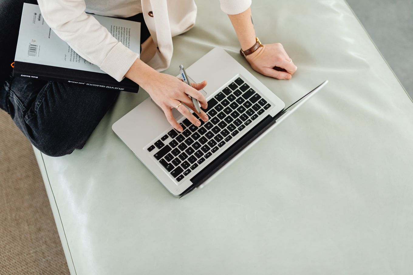 Freelancer checking work on a laptop with a pen in hand and a notebook on their lap