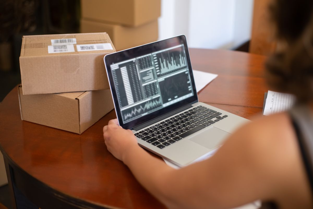 Small business owner reviewing sales charts on a laptop beside packed shipping boxes