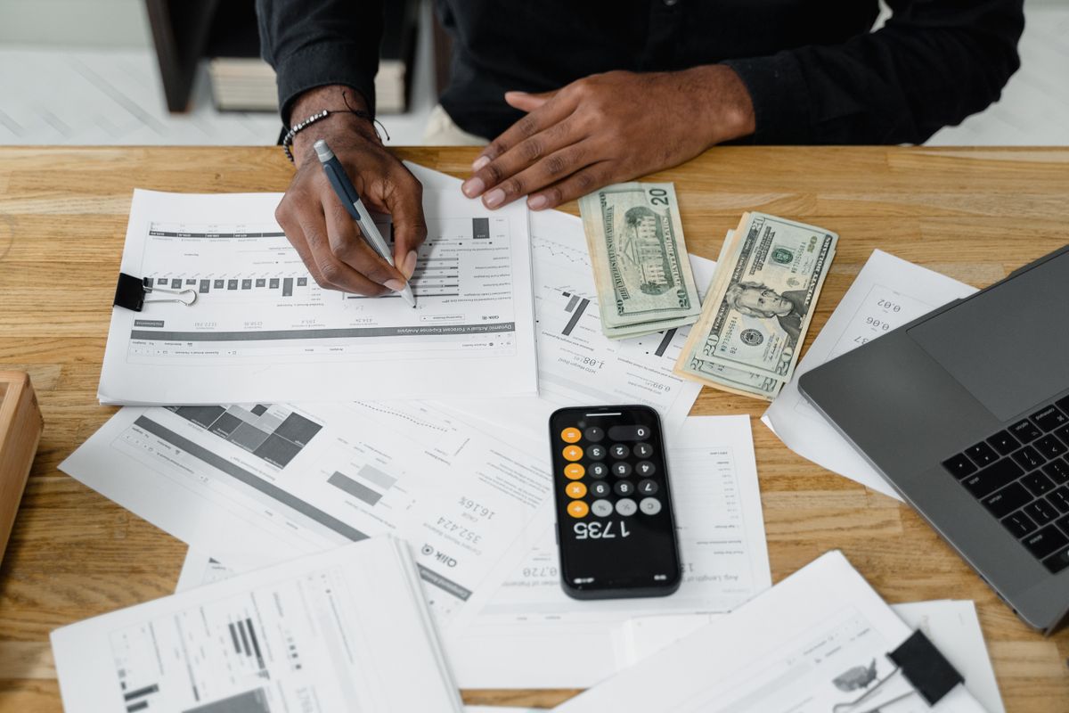 Man working on financial reports with calculator, money, and laptop on a desk
