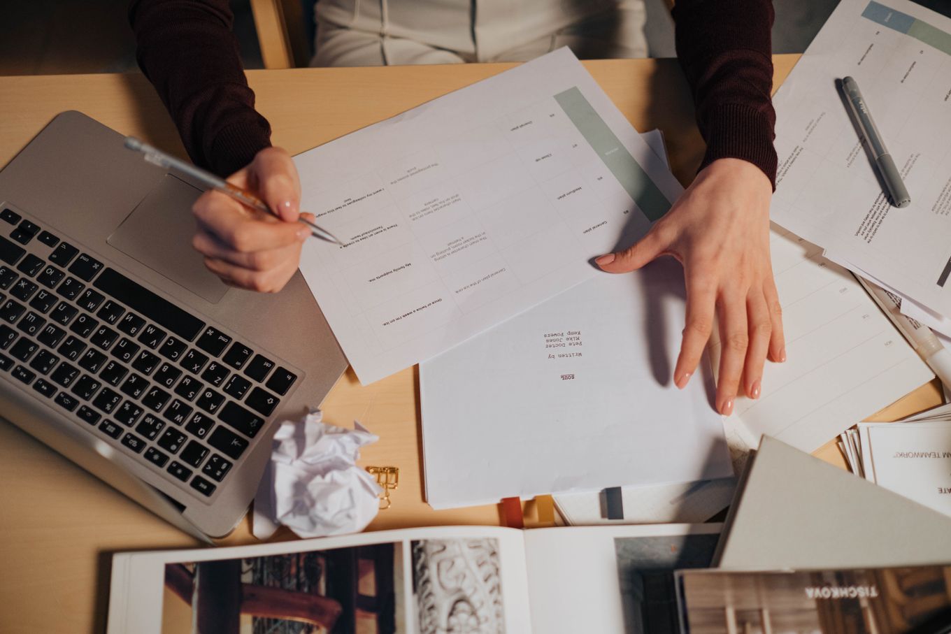 Freelancer going through printed paperwork with a pen beside an open laptop