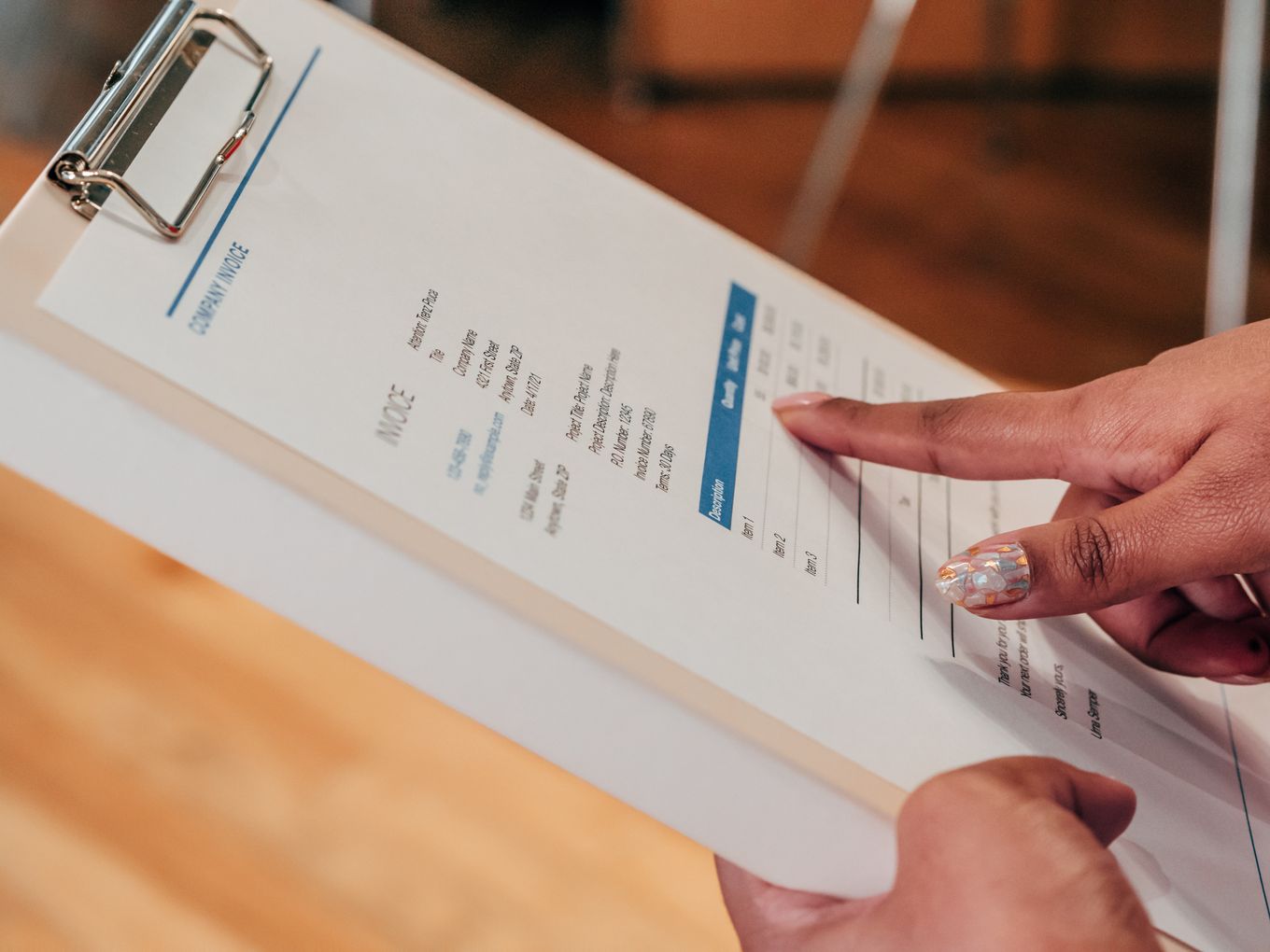 Finger pointing at a line item on a printed invoice clipped to a clipboard