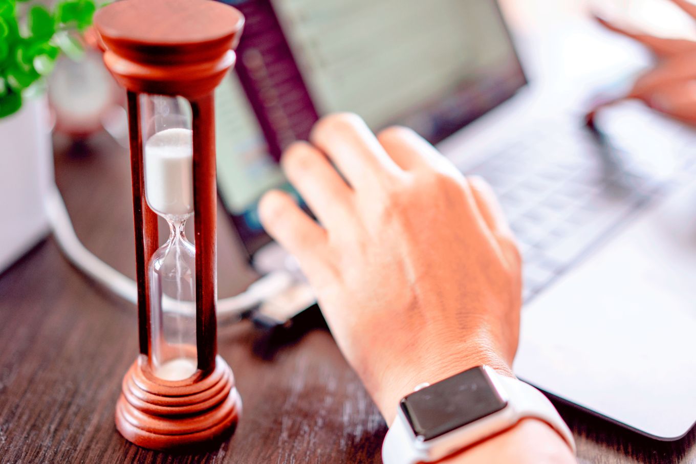 Hourglass on a desk beside a hand typing on a laptop