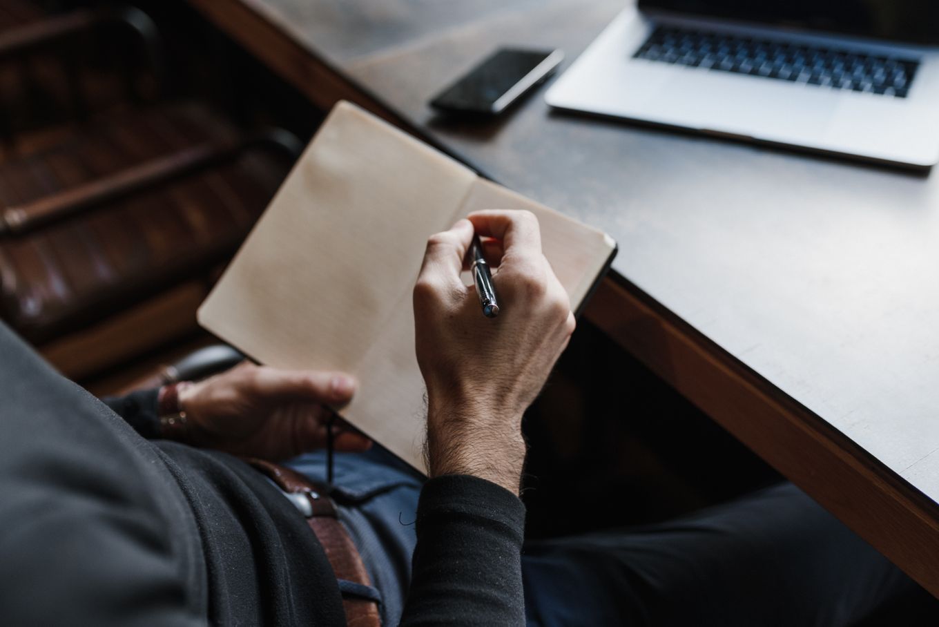 Freelancer writing notes in a notebook next to a laptop and phone