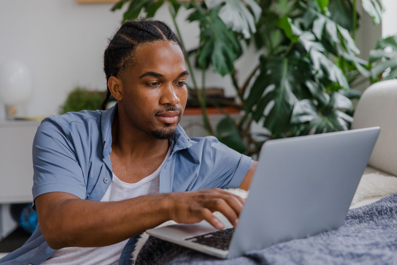 Freelancer working on a laptop at home beside a large monstera plant