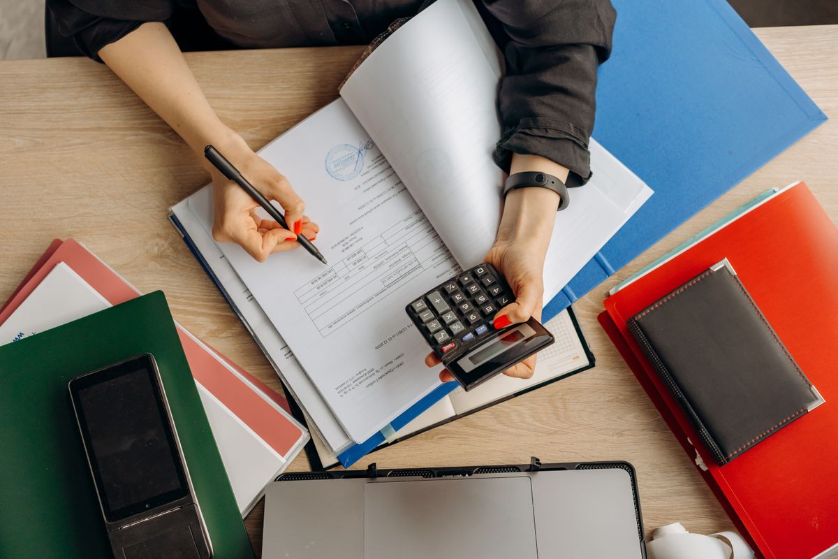 Person working through financial documents with a calculator and ring binders