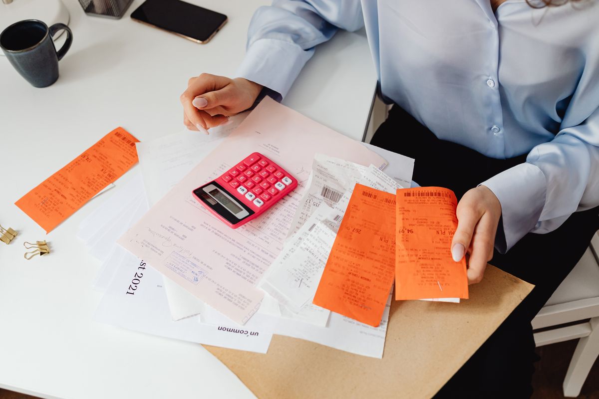 Person sorting through paper receipts with a calculator on a desk