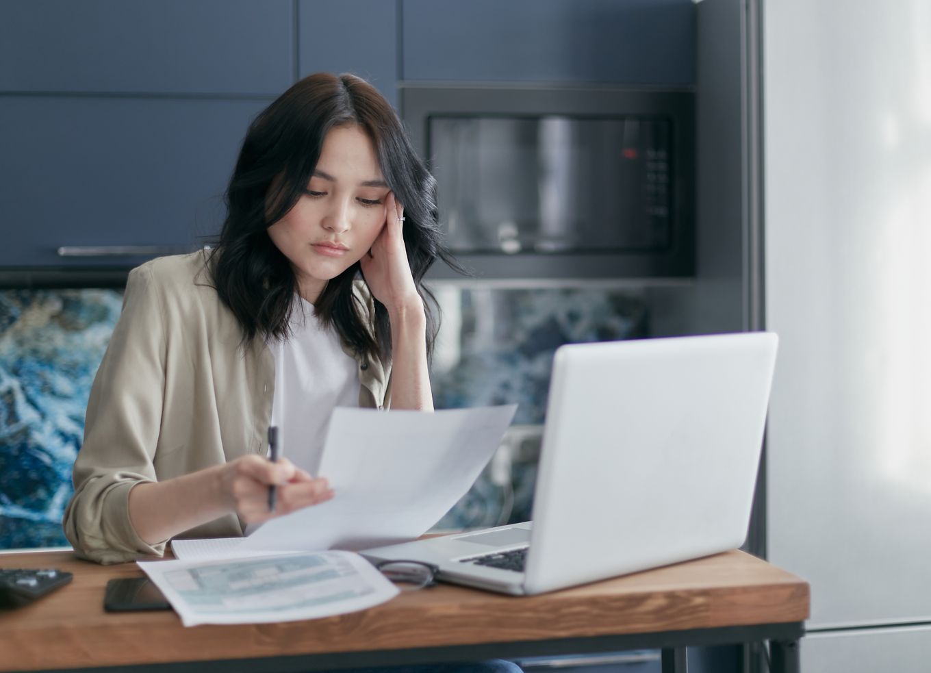 Woman at a home office desk frowning at a bill in front of her laptop