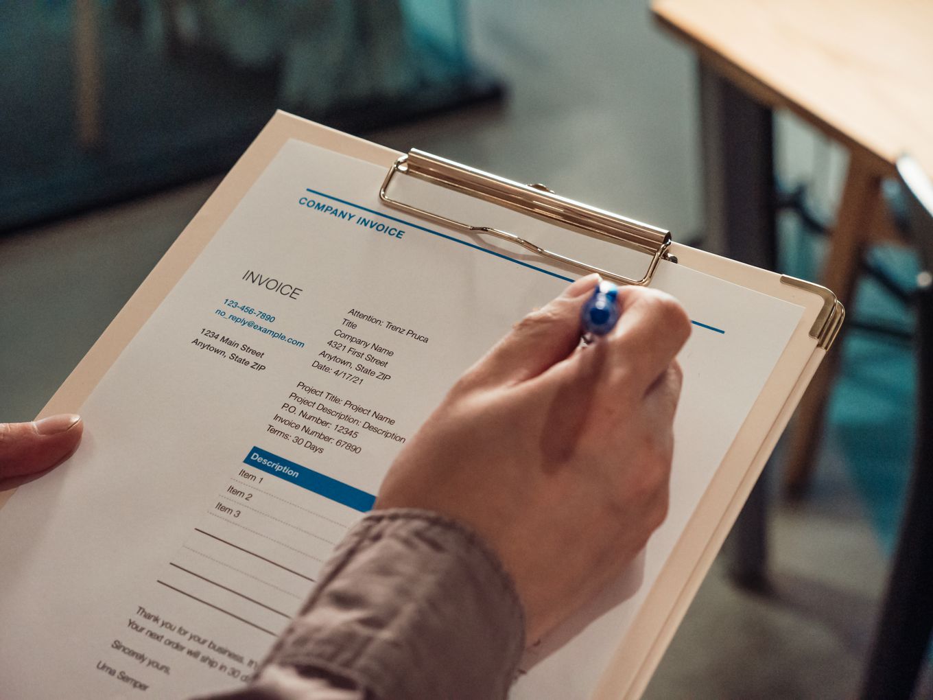 Person checking a company invoice on a clipboard with a pen